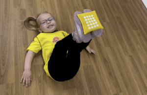 Football confidence for toddlers. Image shows girl laying down balancing a bean bag on her feet in a Socatots class. 