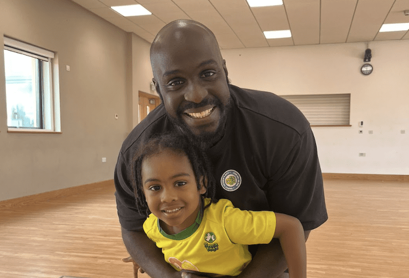 Toddler fun learning. Image shows a dad and his child at a Socatots class smiling to camera. 